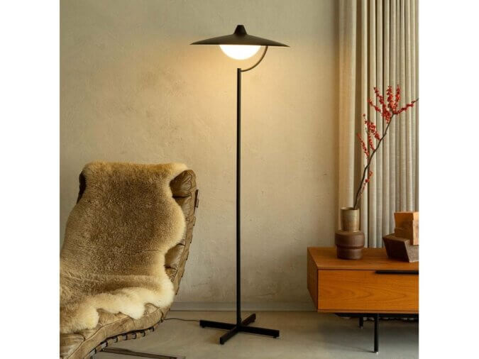 Lampada da Terra Biny Floor accesa e in una stanza con una poltrona, una madia ed un ramo con foglie.