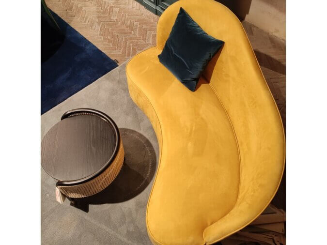 Curved Sofa giallo visto dall'alto con un cuscino blu su un tappeto blu cielo. Tavolino davanti.