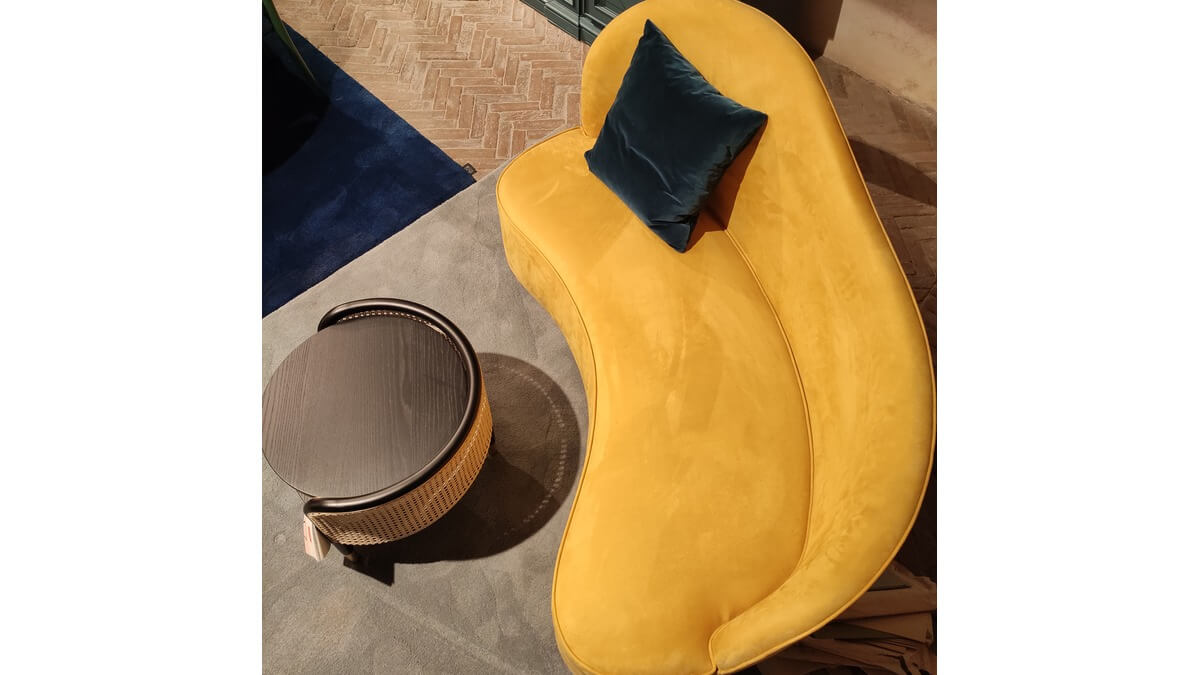 Curved Sofa giallo visto dall'alto con un cuscino blu su un tappeto blu cielo. Tavolino davanti.