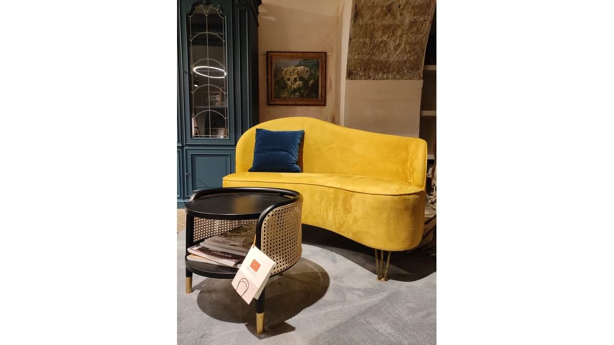 Curved Sofa giallo con un cuscino blu su un tappeto blu cielo. Tavolino davanti ed una madia blu dietro.