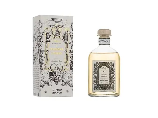 Una bottiglia in vetro di Divino Bianco Profumatore d'ambiente, riempita di liquido giallo, fornita di etichetta decorativa e tappo in legno. Accanto la sua confezione decorata da illustrazioni bianco, nero e oro.