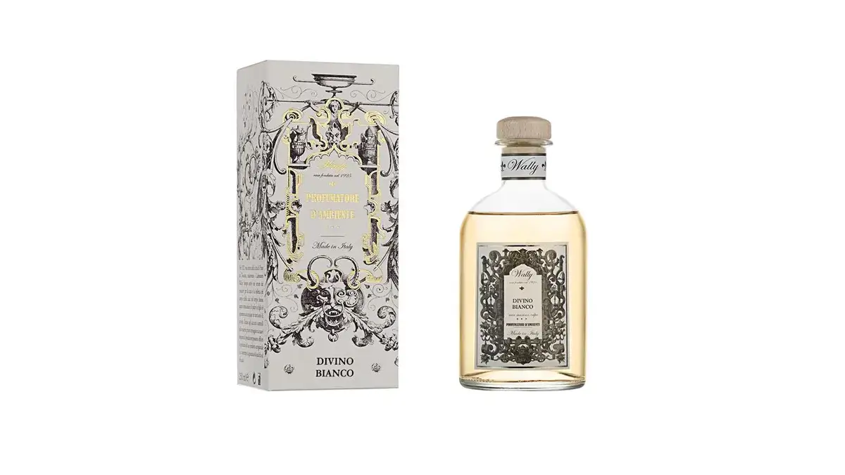Una bottiglia in vetro di Divino Bianco Profumatore d'ambiente, riempita di liquido giallo, fornita di etichetta decorativa e tappo in legno. Accanto la sua confezione decorata da illustrazioni bianco, nero e oro.