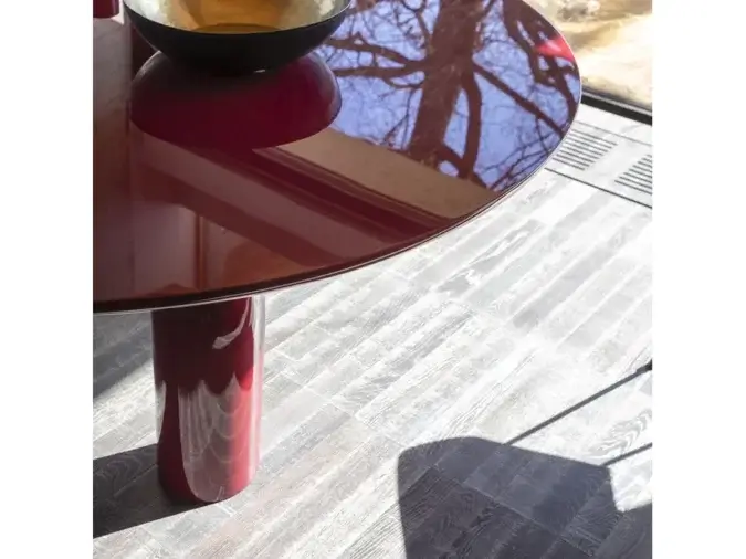 Dettagli del piano del Tavolo Elephante Rosso lucido con sopra degli oggetti e l'ombra di una sedia.