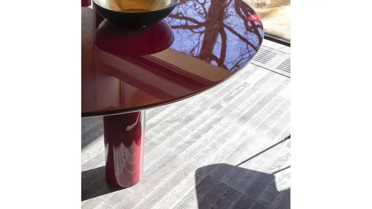 Dettagli del piano del Tavolo Elephante Rosso lucido con sopra degli oggetti e l'ombra di una sedia.