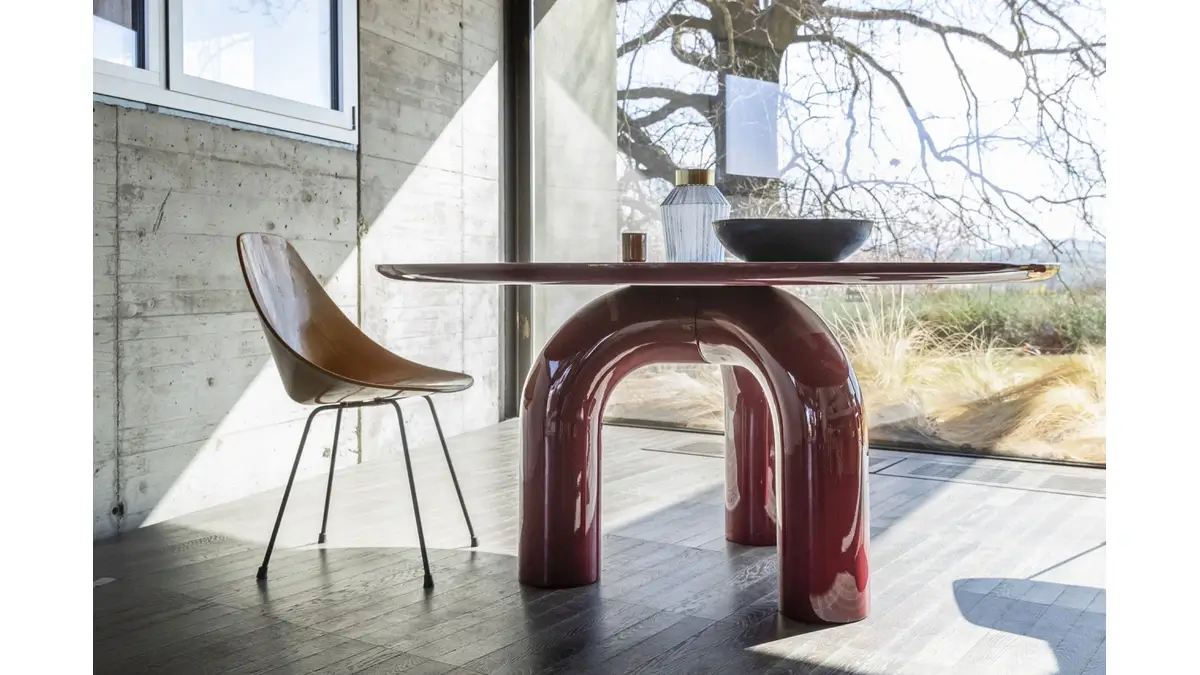 Tavolo Elephante rosso lucido in sala da pranzo moderna con una sedia marrone accanto a una grande finestra con vista sugli alberi spogli.