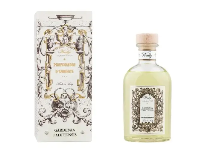Una bottiglia in vetro di Gardenia Tahitensis Profumatore d'ambiente, riempita di liquido giallo, fornita di etichetta decorativa e tappo in legno. Accanto la sua confezione decorata da illustrazioni bianco, nero e oro.