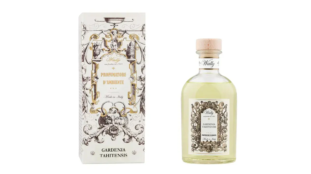 Una bottiglia in vetro di Gardenia Tahitensis Profumatore d'ambiente, riempita di liquido giallo, fornita di etichetta decorativa e tappo in legno. Accanto la sua confezione decorata da illustrazioni bianco, nero e oro.