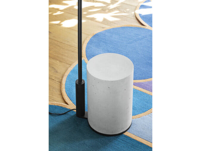 Base in calcestruzzo bianco della lampada da terra Ozz Floor con filo nero su un tappeto blu.
