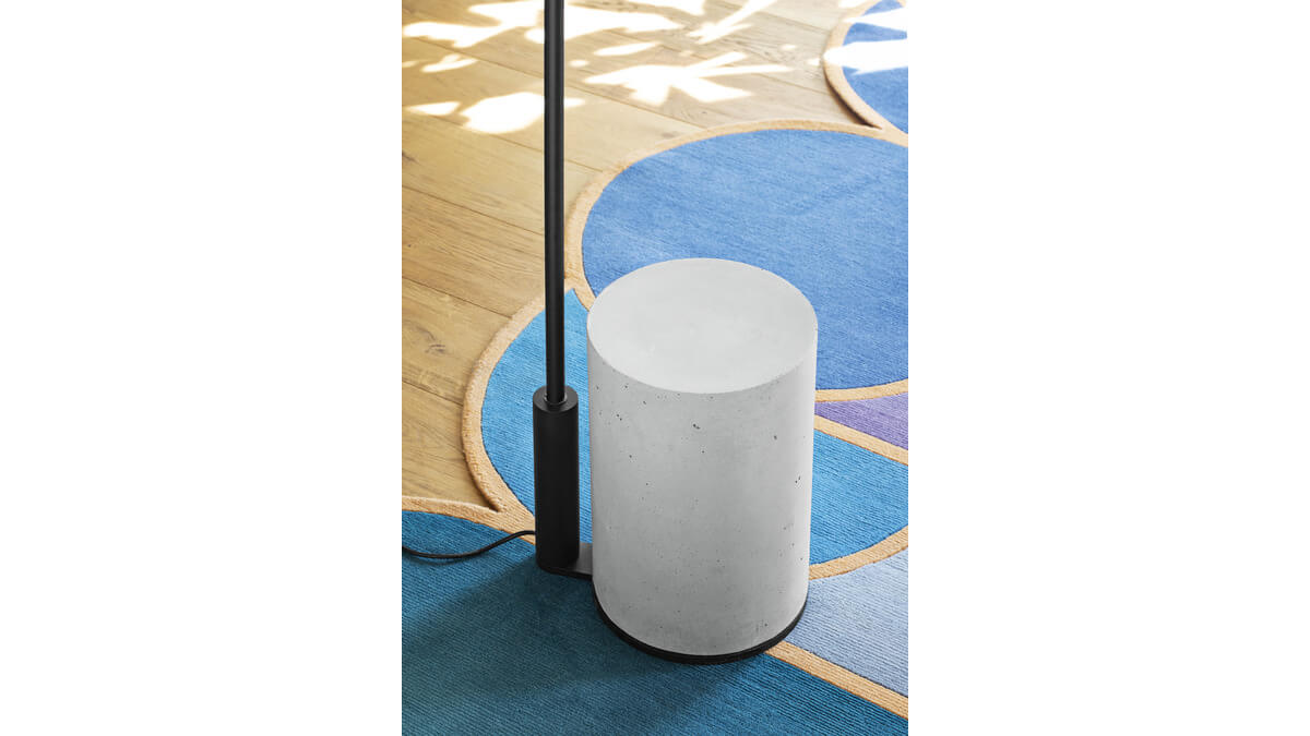 Base in calcestruzzo bianco della lampada da terra Ozz Floor con filo nero su un tappeto blu.