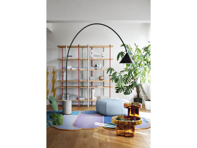 Lampada da Terra Ozz Floor nera con base in calcestruzzo in una stanza con tavolini orange soda, tappeto, libreria, pianta ed un pouf.