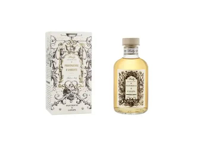 Una bottiglia in vetro di Patchouli E Canapa Profumatore d'ambiente, riempita di liquido giallo ambra, fornita di etichetta decorativa e tappo in legno. Accanto la sua confezione decorata da illustrazioni bianco, nero e oro.