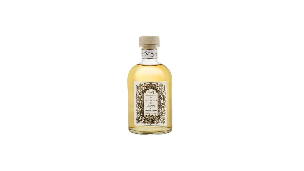 Una bottiglia in vetro di Patchouli E Canapa Profumatore d'ambiente, riempita di liquido giallo ambra, fornita di etichetta decorativa e tappo in legno.