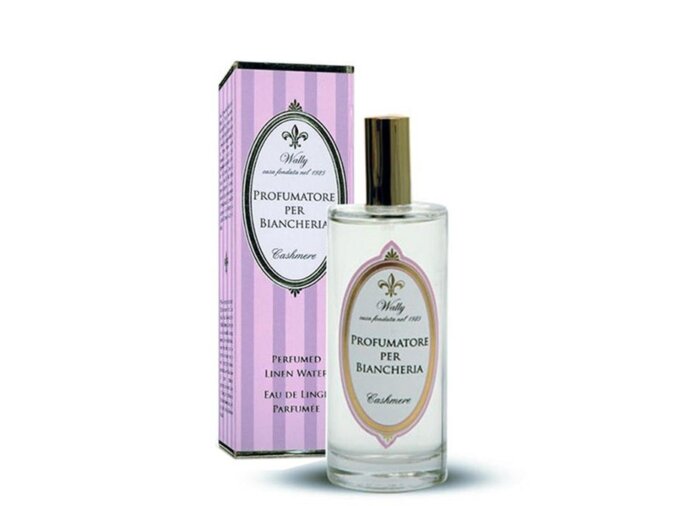 Una bottiglia in vetro di Profumatore per biancheria Cashmere riempita di liquido trasparente, fornita di etichetta decorativa. Accanto la sua confezione decorata da illustrazioni color viola, lillà e bianco.