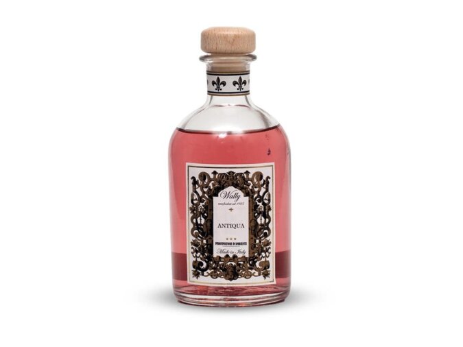 Una bottiglia in vetro di Antiqua Profumatore d'ambiente, riempita di liquido color rosa, fornita di etichetta decorativa e tappo in legno.