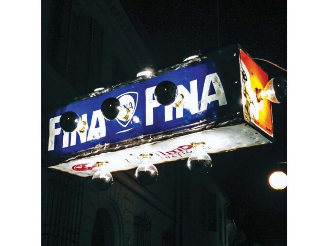 Pendant Lamp Astro in lamiera di bidone blu-rossa e bianca. La lampada è accessa ed è situatata in una strada di notte.