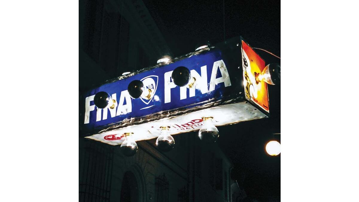Pendant Lamp Astro in lamiera di bidone blu-rossa e bianca. La lampada è accessa ed è situatata in una strada di notte.