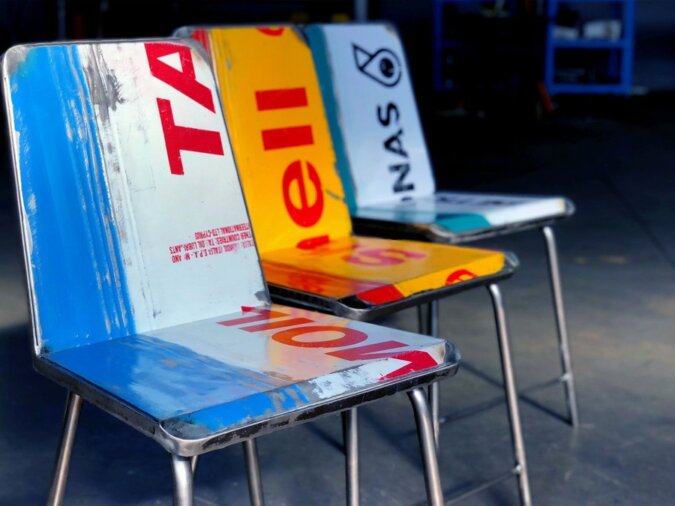 Primo piano di tre Avio Sedie in lamiera di bidone blu-bianco, giallo-rosso e verde-bianco di varie aziende. Sono poste in un garage.