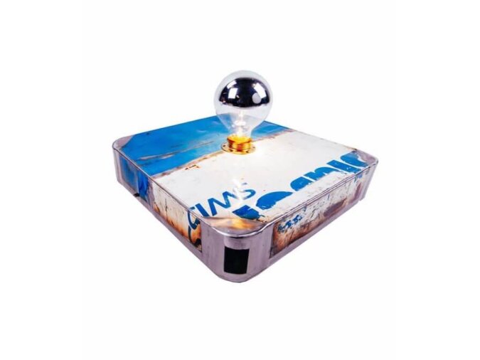 Vista angolare della lampada da tavolo Block Lamp in lamiera di bidone bianca e blu, dotata di una lampadina accesa.