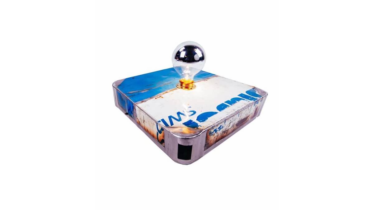 Vista angolare della lampada da tavolo Block Lamp in lamiera di bidone bianca e blu, dotata di una lampadina accesa.