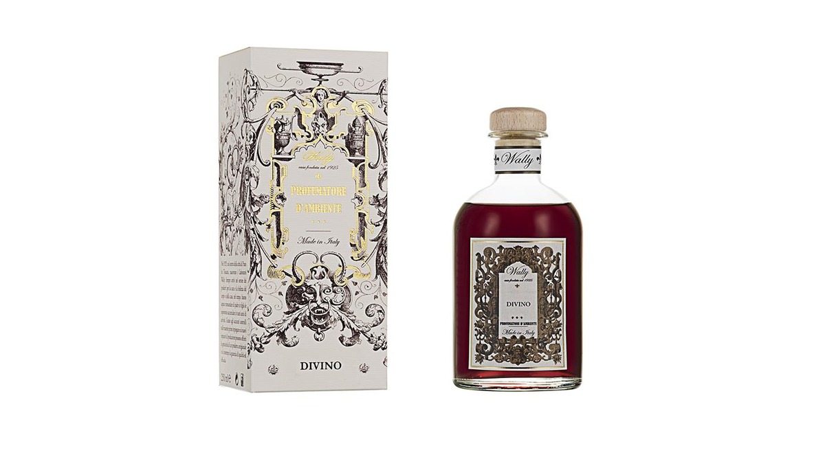Una bottiglia in vetro di Divino Profumatore d'ambiente, riempita di liquido rosso, fornita di etichetta decorativa e tappo in legno. Accanto la sua confezione decorata da illustrazioni bianco, nero e oro.