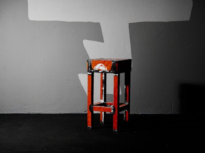 Doeby Sgabello in lamiera di bidone rosso posto in una stanza con pavimento nero e muro in cemento.