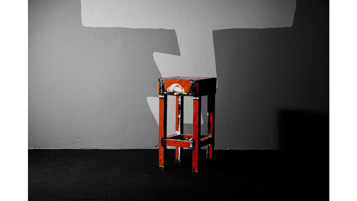 Doeby Sgabello in lamiera di bidone rosso posto in una stanza con pavimento nero e muro in cemento.