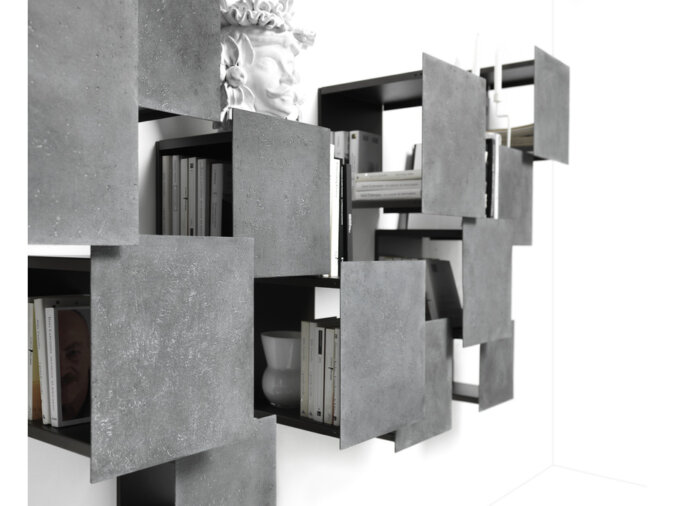 Dettagli della composizione di scaffali modulari DPI libreria a parete in finitura grigio lava con libri ed oggetti poggiati all'interno dei vari moduli.