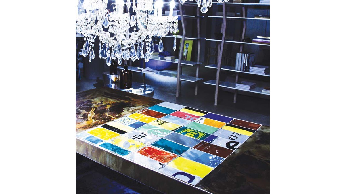 Dettagli colorati del Tavolo Easytable in lamiera di bidone. Sullo sfondo una libreria in ferro e sopra un Pendant Lamp in cristallo.