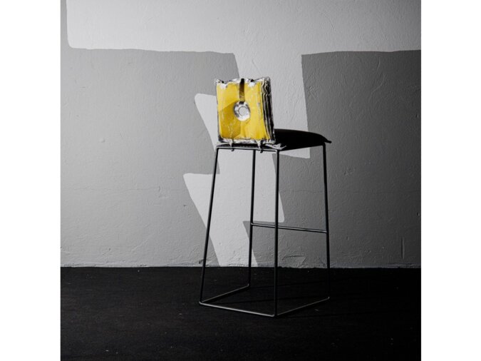 Retro di Elio sgabello in lamiera di bidone giallo in una stanza con pavimento nero e muro in cemento grigio.