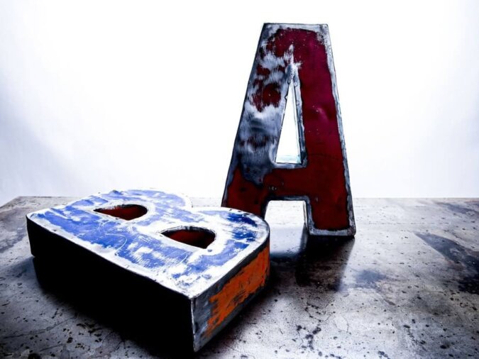 Lettere A e B di Font oggetti in lamiera di bidone di colore rosso e blu, appoggiati su un piano in ferro.