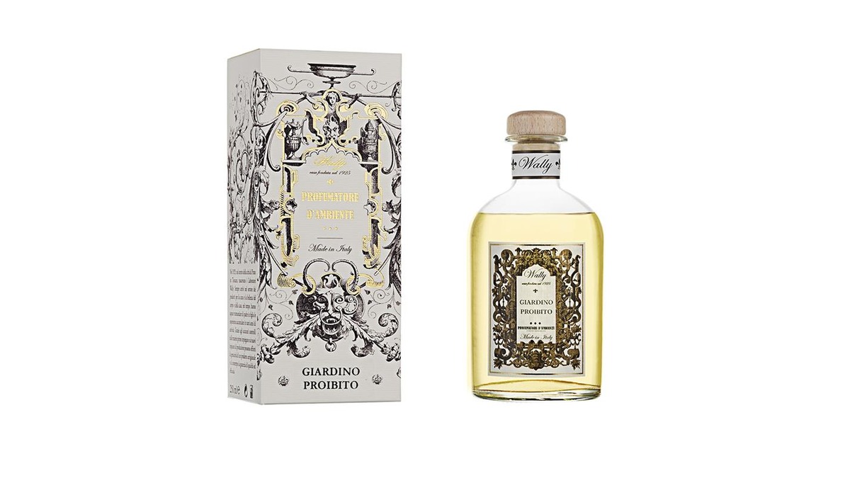 Una bottiglia in vetro di Giardino Proibito Profumatore d'ambiente, riempita di liquido giallo chiaro, fornita di etichetta decorativa e tappo in legno. Accanto la sua confezione decorata da illustrazioni bianco, nero e oro.