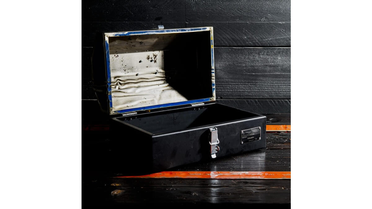 Dettagli interni della cassetta degli attrezzi GT Toolbox in lamiera di bidone appoggiata su un piano di legno nero con fasce arancioni.