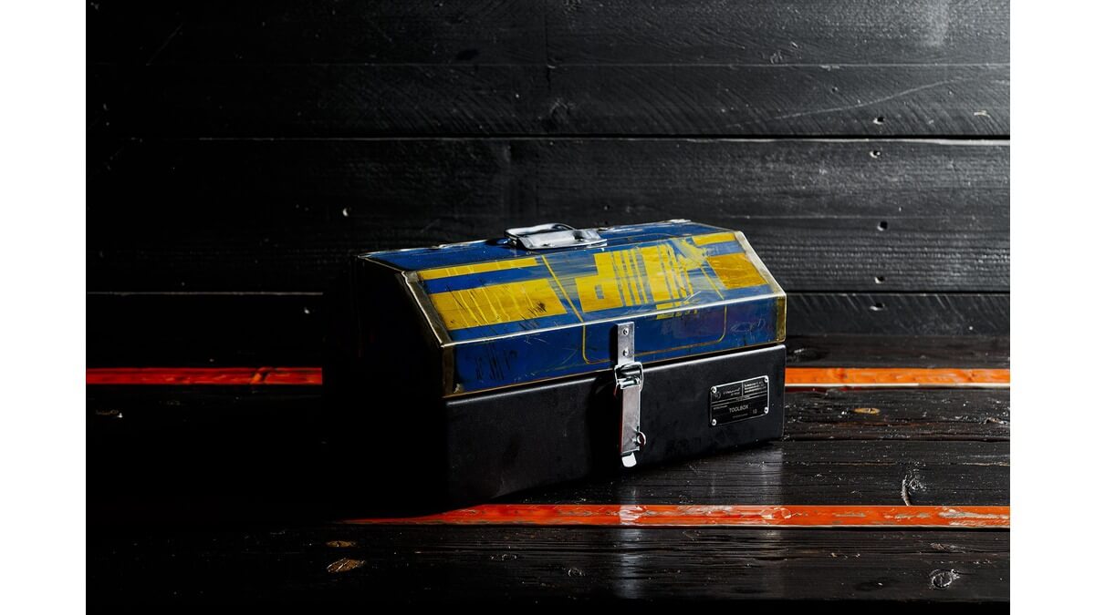 Cassetta degli attrezzi GT Toolbox in lamiera di bidone appoggiata su un piano di legno nero con fasce arancioni.