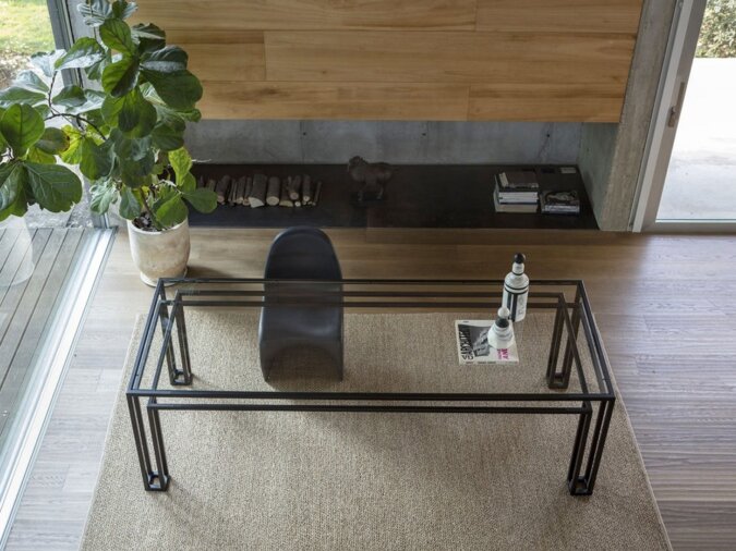 Tavolo Hotline in uno spazio abitativo moderno con struttura in metallo, una grande pianta in vaso e un arredamento minimalista su un tappeto beige strutturato.
