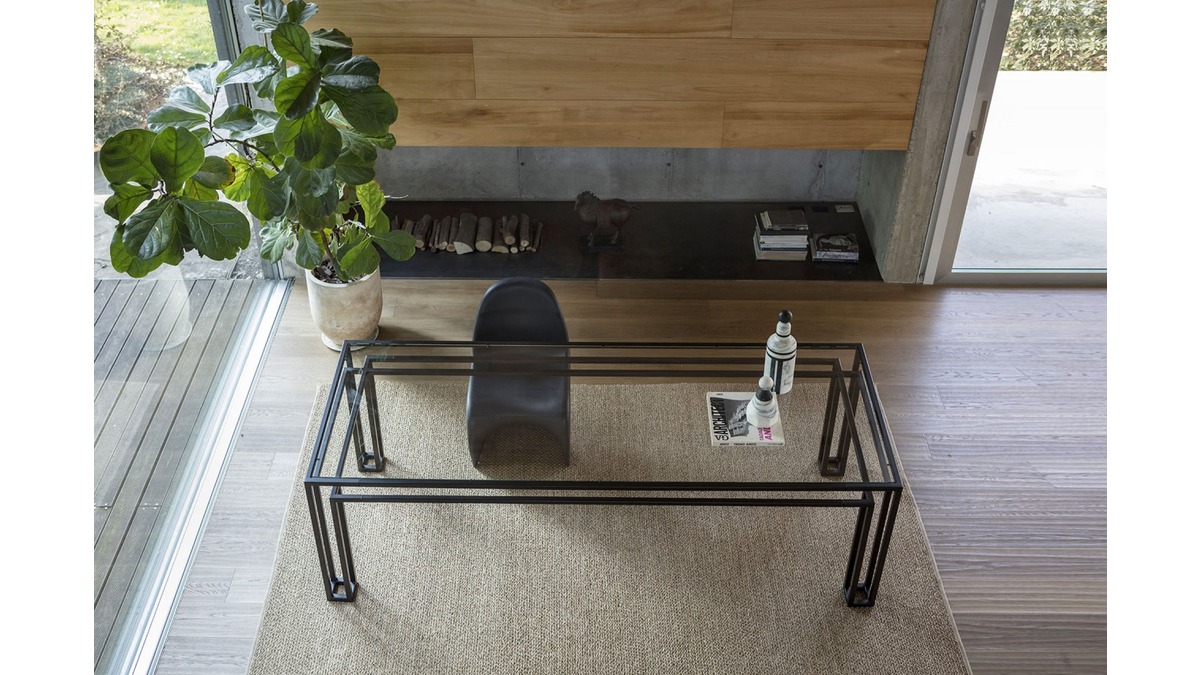 Tavolo Hotline in uno spazio abitativo moderno con struttura in metallo, una grande pianta in vaso e un arredamento minimalista su un tappeto beige strutturato.