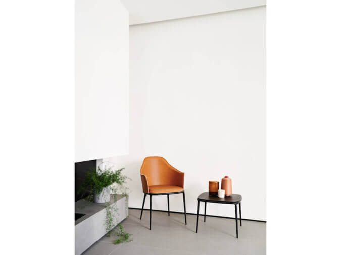 Lea Sedia in cuoio arancione e struttura metallo nera in stanza bianca con affianco tavolino nero.
