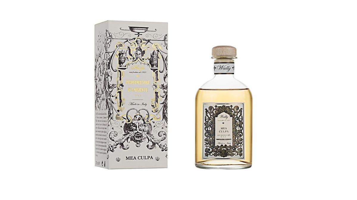 Una bottiglia in vetro di Mea Culpa Profumatore d'ambiente, riempita di liquido giallo, fornita di etichetta decorativa e tappo in legno. Accanto la sua confezione decorata da illustrazioni bianco, nero e oro.