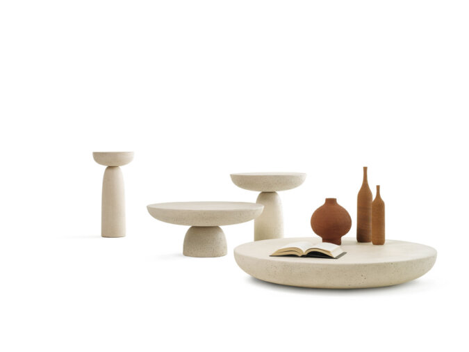 Tavolini Olo coffee tables in cemento colore avorio in varie dimensioni. Sul tavolino più largo sono appoggiate delle bottiglie ed un libro.