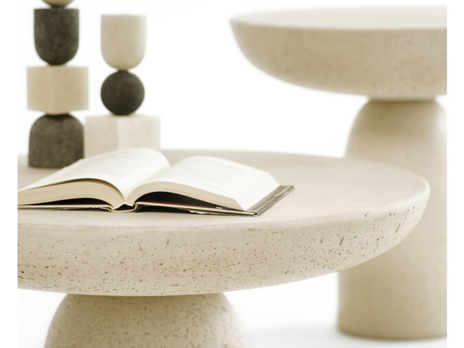 Un primo piano dei tavolini Olo in cemento di colore Avorio. Su un tavolino sono appoggiati un libro aperto e due sculture. Si vedono i dettagli porosi dell'elemento.