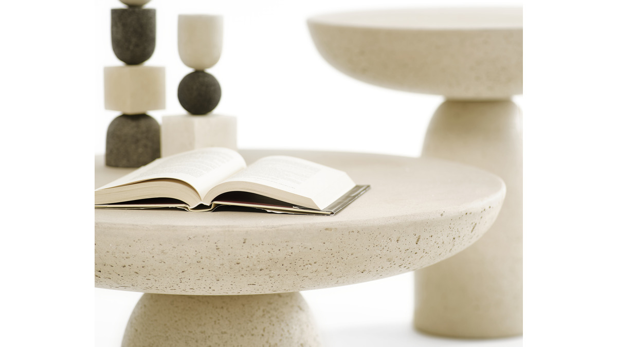 Un primo piano dei tavolini Olo in cemento di colore Avorio. Su un tavolino sono appoggiati un libro aperto e due sculture. Si vedono i dettagli porosi dell'elemento.