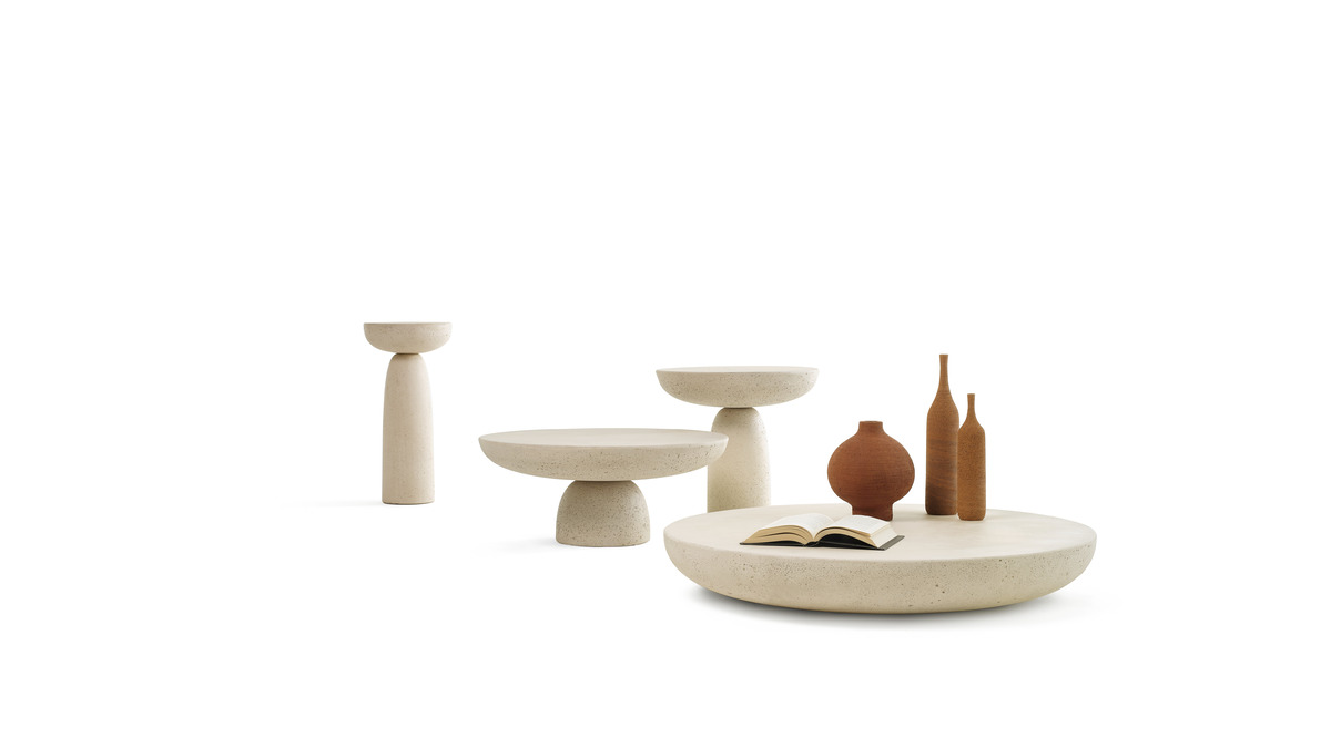 Tavolini Olo coffee tables in cemento colore avorio in varie dimensioni. Sul tavolino più largo sono appoggiate delle bottiglie ed un libro.
