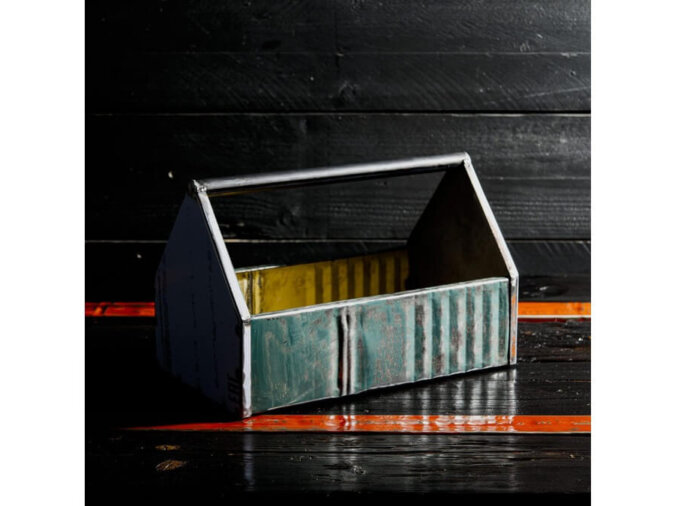 Cassetta degli attrezzi Petrolhead Toolbox in lamiera di bidone, appoggiata su un piano di legno nero e arancione.