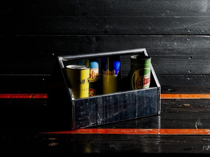 Cassetta degli attrezzi Petrolhead Toolbox in lamiera di bidone con contenitori di latta all'interno, appoggiata su un piano di legno nero e arancione.