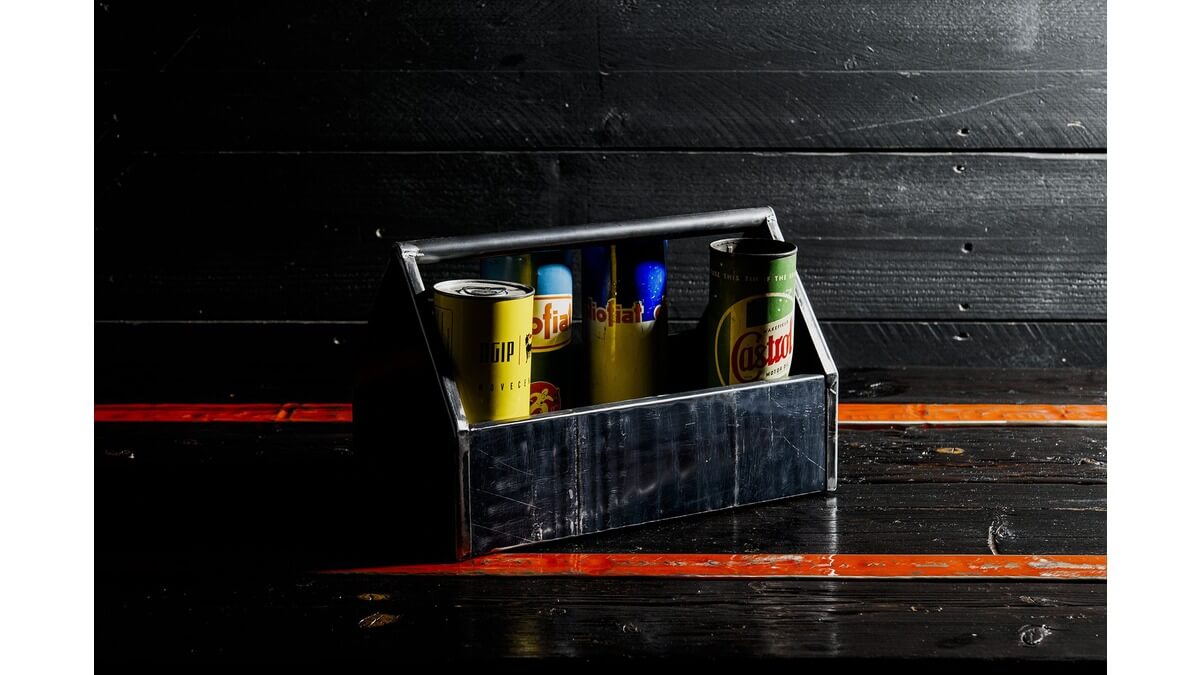 Cassetta degli attrezzi Petrolhead Toolbox in lamiera di bidone con contenitori di latta all'interno, appoggiata su un piano di legno nero e arancione.