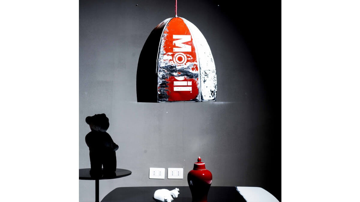 Pendant Lamp Rugby in lamiera di bidone bianca e rosso con scritta Mobil in living room con un tavolo nero, sul quale sono poggiati un vaso rosso e altri oggetti.