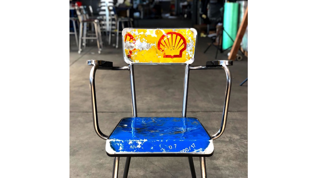Dettagli della sedia Secca con braccioli in lamiera di bidone con seduta blu e schienale giallo con simbolo conchiglia. La sedia è situata in un garage.