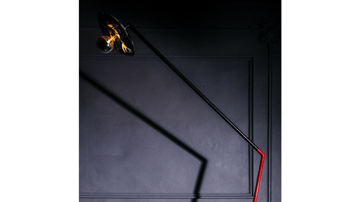 Lampada da terra Settanta in lamiera di bidone rossa e nera con lampadina spenta. Posta in una stanza poco illuminata.