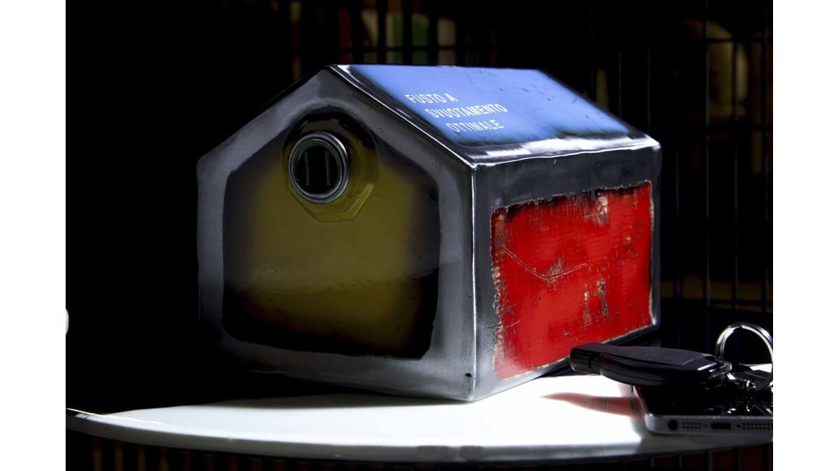 Salvadanaio Vad House in Lamiera di bidone a forma di casetta di colore giallo, blu,rosso e acciaio, appoggiato su un piano in marmo bianco.