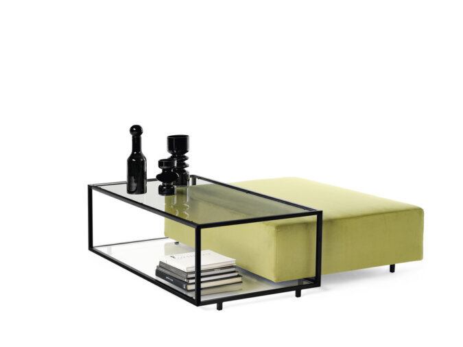 Zoom Coffee table in vetro con cornice nera, ornato con bottiglie decorative e libri, abbinato a un pouf verde muschio.