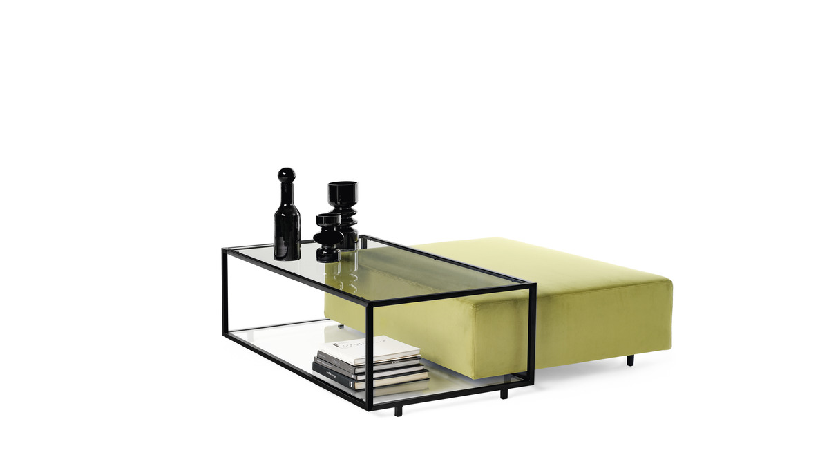 Zoom Coffee table in vetro con cornice nera, ornato con bottiglie decorative e libri, abbinato a un pouf verde muschio.